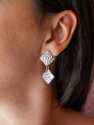 Είναι ιδιαίτερα σκουλαρίκια με ανάγλυφη υφή που θυμίζει τη ροή των φυσικών μοτίβων της πέτρας. Κατασκευασμένα από λαμπερό ασημί ατσάλι, διαθέτουν δύο συνδεδεμένους ρόμβους με οργανικό, σφυρήλατο φινίρισμα που αντανακλά το φως με μοναδικό τρόπο. Ελαφριά και εντυπωσιακά.