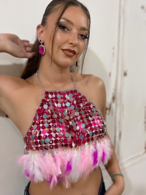 Halter top με φούξια παγιέτες. Διακοσμημένο με φτερά και εντυπωσιακά κρύσταλλα. Για εμφανίσεις που απαιτούν λάμψη και ενέργεια. Μπορεί να συνδυαστεί με τζιν, φούστα, κοστούμι, σκέτο ή πάνω από στράπλες φόρεμα.